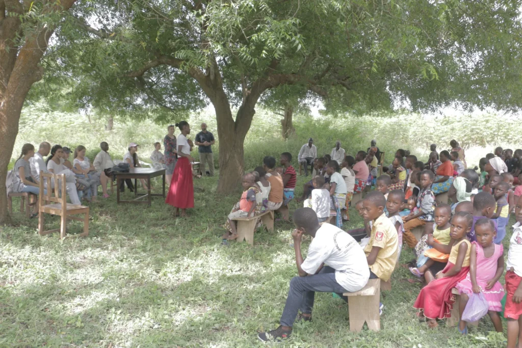 An open-air service under the trees with adults and children gathered to hear the Good News