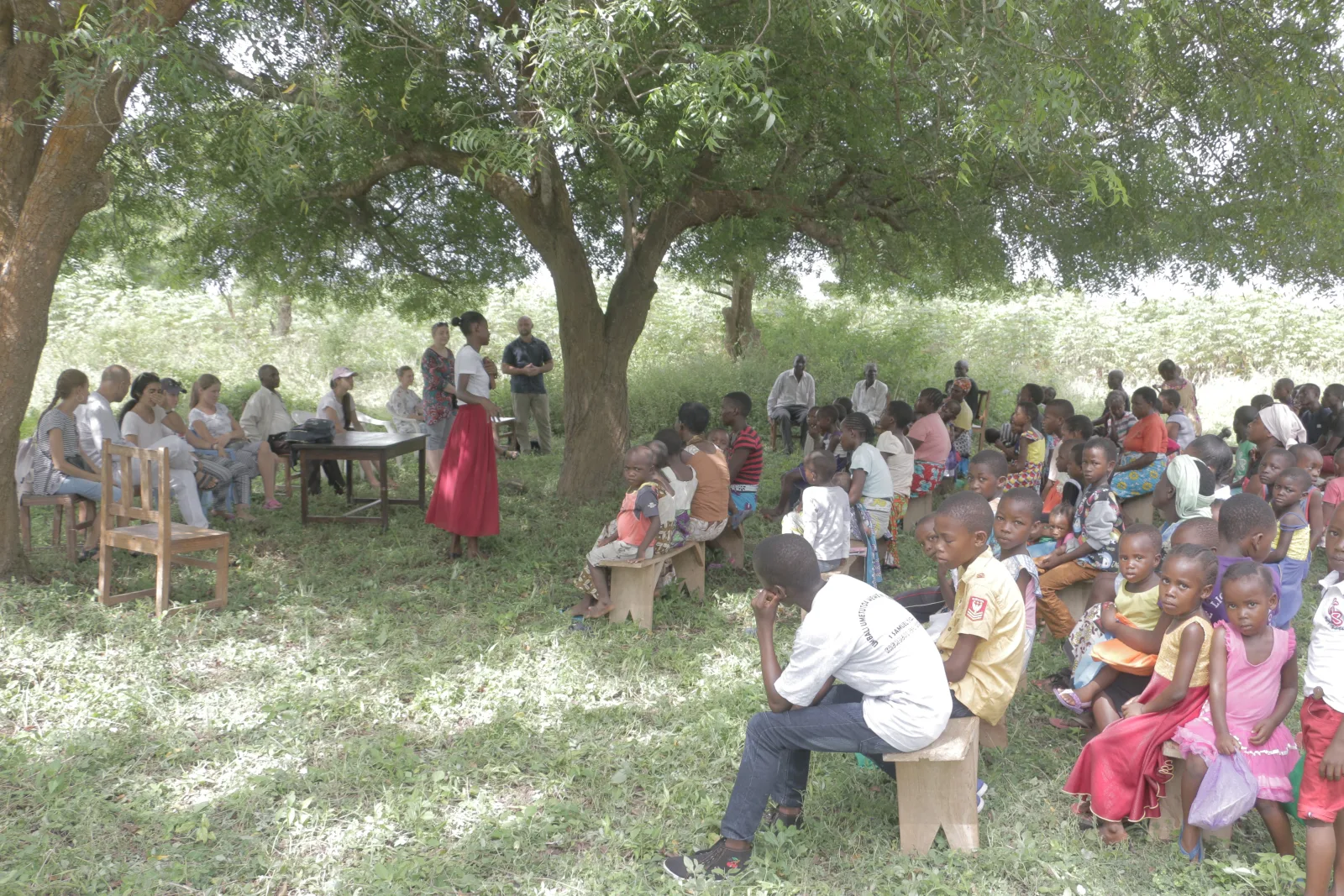 An open-air service under the trees with adults and children gathered to hear the Good News